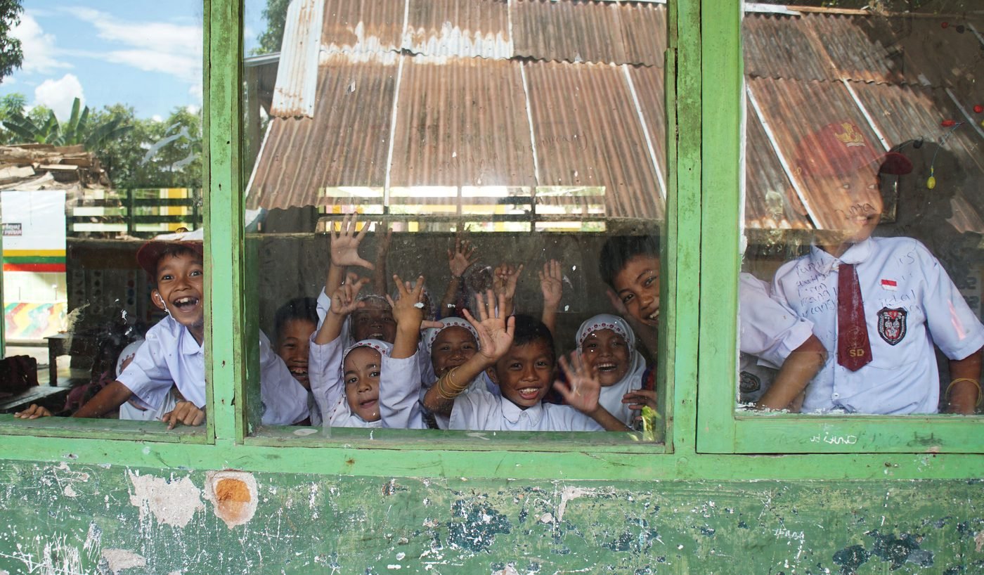 Joyful school children smiling and waving from a classroom window