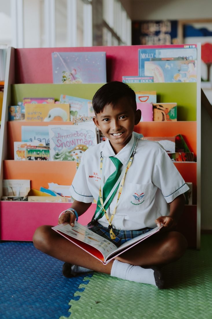 Schoolboy smiling while reading a book in a library