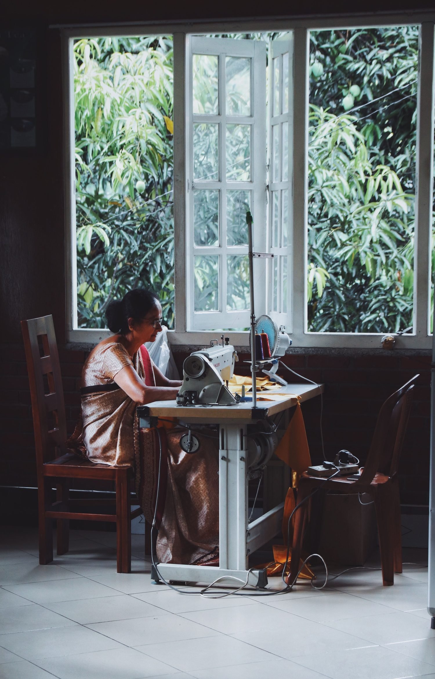 Indian woman tailoring garments at a sewing machine in a bright workspace